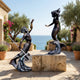 Monumental Classical Triton and Mermaid Bronze Sculpture by Giant Sculptures displayed on a stone terrace overlooking the sea, framed by olive trees.