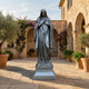 Giant Sculptures Monumental Classical Virgin Mary Bronze Statue 300cm with dark grey-green patina on a stepped plinth in a sunlit Mediterranean stone courtyard.