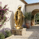 Monumental Classical Virgin Mary Bronze Statue in gold finish by Giant Sculptures, displayed on a stone plinth in a Mediterranean courtyard with lavender.
