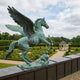 Monumental Classical Winged Horse Bronze Sculpture by Giant Sculptures with verdigris patina, rearing on a parapet overlooking a formal hedge garden.