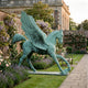 Monumental Classical Winged Horse Bronze Sculpture by Giant Sculptures in verdigris patina, mid-stride with wings raised, displayed in a walled rose and wisteria garden.
