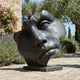 Monumental Contemporary Abstract Face Fragment Bronze Sculpture by Giant Sculptures on a stone terrace beside lavender, olive trees, and a weathered wall.