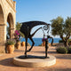 Monumental Contemporary Abstract Horse and Girl Bronze Sculpture by Giant Sculptures on a stone terrace, dark patina figures framed by an arch, olive trees, and sea view.