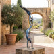 Monumental Contemporary Acrobatic Figures Bronze Sculpture by Giant Sculptures, two patinated bronze acrobats stacked in handstands on a stone plinth in a Mediterranean courtyard.