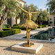 Monumental Contemporary Ballerina Dancer Bronze Sculpture by Giant Sculptures in polished gold, arms outstretched on a circular base beside a poolside garden.