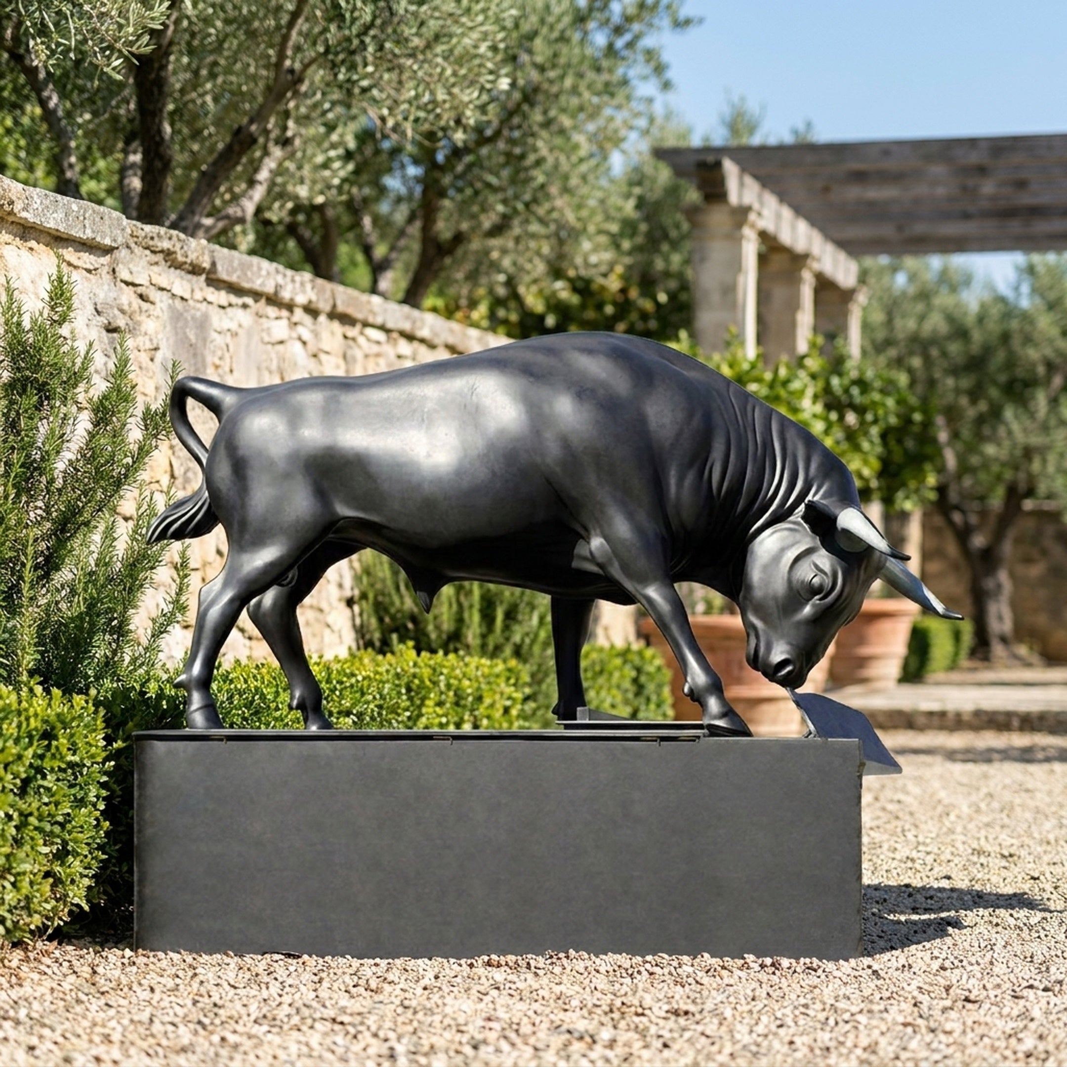 Giant Sculptures Monumental Charging Bull bronze with matte black patina on a dark granite plinth, head lowered, displayed in a Mediterranean garden courtyard.