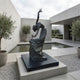 Monumental Contemporary Dancing Female Figure Bronze Sculpture by Giant Sculptures, arched backward with raised hand, on a granite plinth in a concrete courtyard.