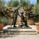 Giant Sculptures' Monumental Contemporary Female Soldier Memorial Bronze in a garden, two soldiers at a battlefield cross with US flag against a stone wall.