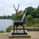 Rear view of Giant Sculptures' Monumental Contemporary Figure on Grand Piano Bronze Sculpture, bronze nude with arms raised on a black long-legged piano by a lake.