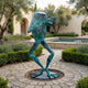 Monumental Contemporary Flute-Playing Frog Bronze Sculpture by Giant Sculptures with verdigris patina, posed mid-stride on a paved garden path beside lavender.