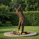 Giant Sculptures Monumental Contemporary Golfer Bronze Sculpture 310cm shown mid follow-through on a pale stone circular plinth with floral tributes, set on a lawn.