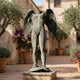 Monumental Contemporary Headless Winged Figure Bronze Sculpture by Giant Sculptures with verdigris patina, displayed in a Mediterranean courtyard with olive trees.