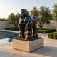 Monumental Contemporary Rotund Horse Bronze Sculpture by Giant Sculptures on a low travertine plinth beside a pool, framed by olive trees and clipped hedges.