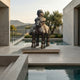 Monumental Contemporary Rotund Rider and Horse Bronze Sculpture by Giant Sculptures on a travertine plinth beside a concrete poolside terrace with hillside views.