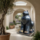 Monumental Contemporary Rotund Seated Cat Bronze Sculpture in black patina with golden-brown paw highlights, displayed in an arched stone corridor near a fountain.