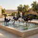 Monumental Contemporary Running Deer Bronze Fountain by Giant Sculptures, dark patinated herd mid-gallop through a stone basin with water jets, olive trees beyond.