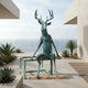 Monumental Contemporary Seated Stag Bronze Sculpture by Giant Sculptures in verdigris patina, seated on a frame on an oceanfront terrace with succulents.