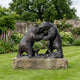 Monumental Fighting Bears Bronze Sculpture by Giant Sculptures, two rearing bears with dark patina on a stone plinth, set in a walled garden with flowers.