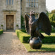 Monumental Heraldic Eagle Bronze Sculpture by Giant Sculptures with wings spread, perched on an orb, set on a gravel path beside a stone manor house.