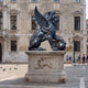Monumental Heraldic Winged Lion Bronze Sculpture by Giant Sculptures, 190cm, seated with spread wings and paw on an orb, on a carved stone plinth in a piazza.