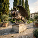 Monumental Heraldic Winged Lion Bronze Sculpture by Giant Sculptures, rearing with wings spread on a stone plinth in a cypress-lined Italianate garden.