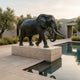 Monumental Life-Size Walking Elephant Bronze Sculpture by Giant Sculptures on a travertine plinth beside a reflecting pool with olive trees and hills behind.