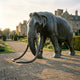 Giant Sculptures Monumental Life-Size Walking Elephant Bronze Sculpture with sweeping tusks and dark patina, set on stone paving before a grand estate at sunrise.