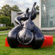 Giant Sculptures Monumental Modern Abstract Cellist Bronze Sculpture 320cm in black patina on a red plinth, displayed on a lawn beside a modern building.