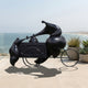 Monumental Modern Abstract Figure and Ice Cream Cart Bronze Sculpture by Giant Sculptures in black patina, displayed on an oceanfront terrace beside potted succulents.