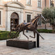 Monumental Modern Abstract Harness Racing Horse and Sulky Bronze Sculpture by Giant Sculptures in dark patina, displayed on a black plinth outside a brick building.