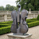 Monumental Modern Double Bass Bronze Sculpture by Giant Sculptures, two overlapping violin forms with scroll detail, on a stone plinth in a formal garden.