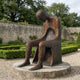 Monumental Modern Seated Figure with Hollow Torso Bronze Sculpture by Giant Sculptures, 220cm, on a circular stone plinth in a walled garden.