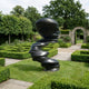 Monumental Modern Spiralling Head Bronze Sculpture by Giant Sculptures in matte black, displayed on a lawn within a formal hedged garden with a stone archway.