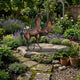 Monumental Rearing and Leaping Arabian Horses Bronze Sculpture by Giant Sculptures, warm brown patina, displayed on a stone slab in a lavender and rose garden.