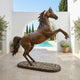 Monumental Rearing Arabian Horse Bronze Sculpture by Giant Sculptures, 260cm, warm brown patina, on a pebble-dressed oval base in a sunlit poolside courtyard.
