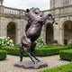 Monumental Rearing Horse Bronze Sculpture by Giant Sculptures at 210cm, reddish-brown patina with darker legs, displayed on gravel in a hedged courtyard garden.