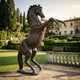 Monumental Rearing Horse Bronze Sculpture by Giant Sculptures, 300cm tall with dark brown patina, displayed on a stone terrace beside a formal villa garden.