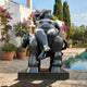 Monumental Rotund Nude Figure and Donkey Bronze Sculpture by Giant Sculptures in black-brown patina, displayed poolside beside bougainvillea and cypress trees.