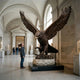 Monumental Spread-Wing Eagle Bronze Sculpture by Giant Sculptures, 350cm, displayed on a stone base in a vaulted museum gallery beside a man for scale.