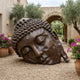 Giant Sculptures Monumental Traditional Buddha Head Bronze Sculpture 150cm reclining on gravel in a Mediterranean courtyard with olive trees and bougainvillea.