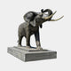 Giant Sculptures Monumental Traditional Bull Elephant Bronze Sculpture 360cm, trunk raised with pale cream tusks, on a two-tiered stone plinth against grey.