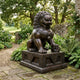 Monumental Traditional Chinese Guardian Lion Bronze Sculpture by Giant Sculptures, seated on a carved plinth with paw on sphere, set in a flowering garden.