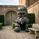Monumental Traditional Chinese Guardian Lion Bronze Sculpture by Giant Sculptures, seated with paw on lattice orb, dark patina, beside a brick courtyard doorway.