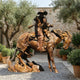 Giant Sculptures Monumental Cowboy and Child on Rearing Horse Bronze Sculpture with warm patina, displayed on gravel in a stone courtyard with olive trees.