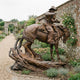 Monumental Traditional Cowboy and Child on Rearing Horse Bronze Sculpture by Giant Sculptures, warm brown patina, displayed on a gravel path in a walled rose garden.