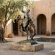 Monumental Traditional Cowboy on Bucking Bronco Bronze Sculpture by Giant Sculptures, displayed on a stone plinth in a sunlit courtyard beside a pool.