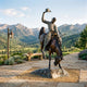 Monumental Traditional Cowboy on Bucking Bronco Bronze Sculpture by Giant Sculptures, rider raising hat as horse rears, displayed on a stone path with mountain views.