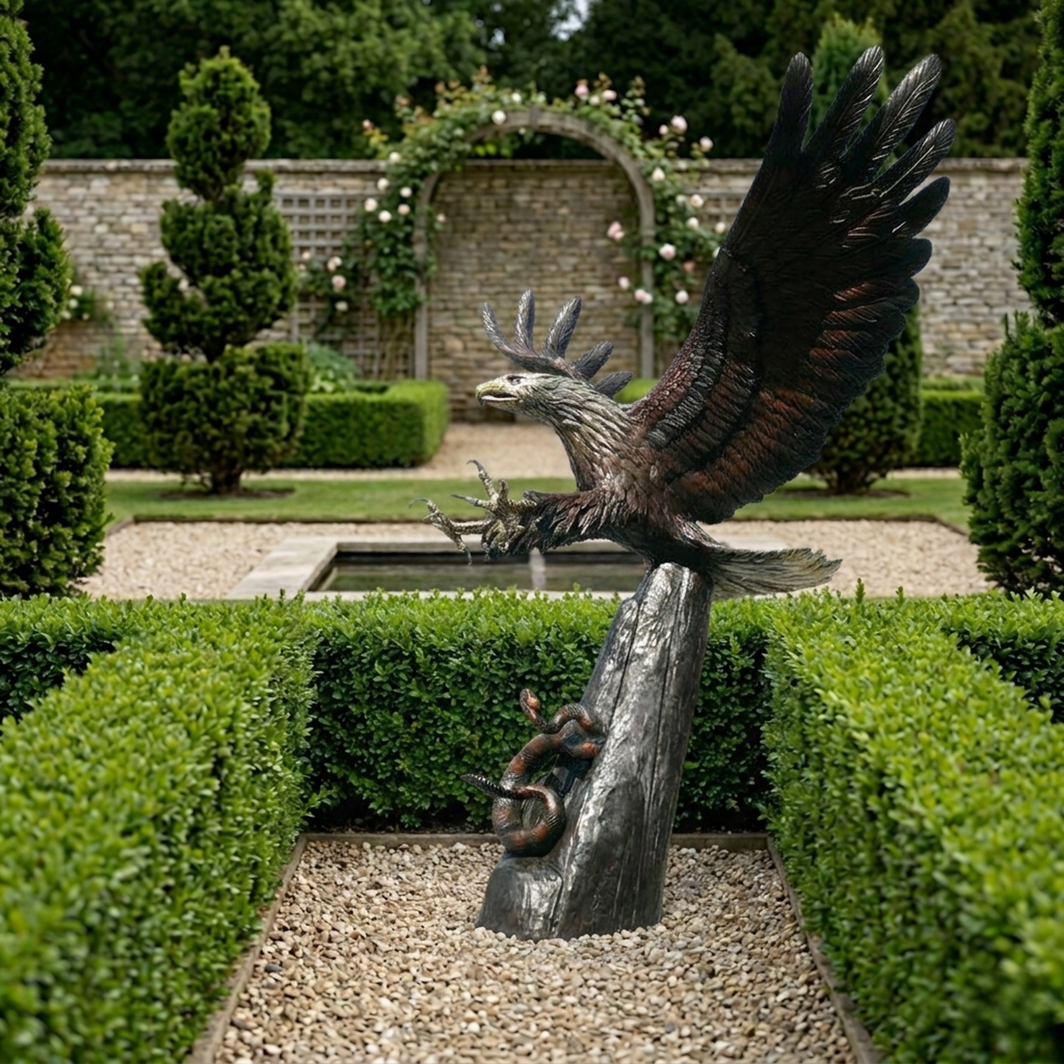Monumental Traditional Eagle Bronze Sculpture by Giant Sculptures with wings raised on a tree-trunk column with coiled snake, set in a formal hedged garden.