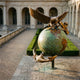 Monumental Traditional Eagle Globe and Anchor Bronze Sculpture by Giant Sculptures, displayed in a stone courtyard with arched colonnades and trimmed hedges.