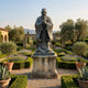 Monumental Traditional Elder Scholar Bronze Statue by Giant Sculptures on a stepped plinth in a formal garden with lavender beds, olive trees, and stone arches.